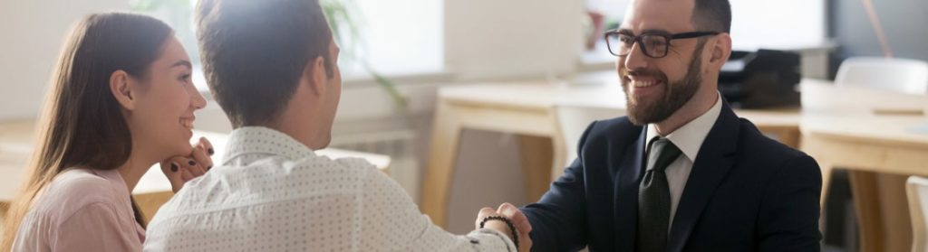 Business man shaking hands with couple from across desk