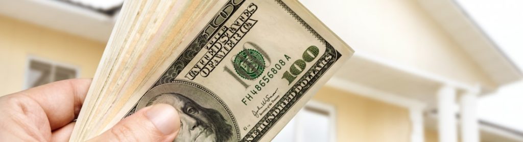 Man's hand holding up $100 dollar bills in front of building