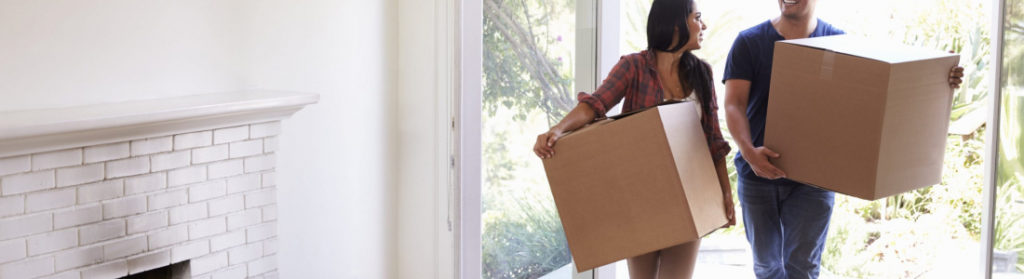 Couple carrying moving boxes inside house