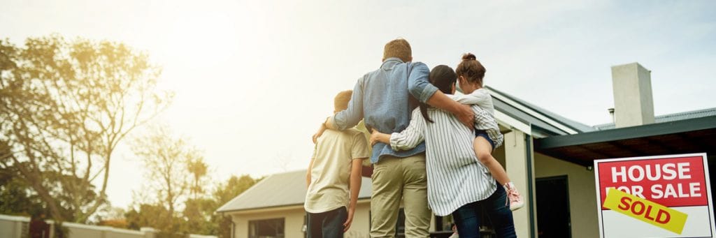 Family standing outside house with "Sold" sign