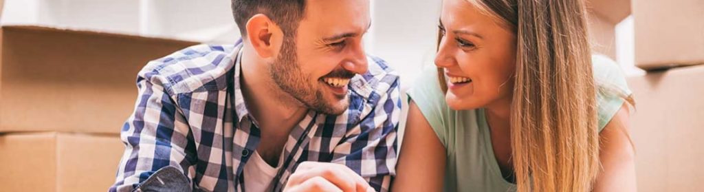 Couple smiling at each other while surrounded by moving boxes