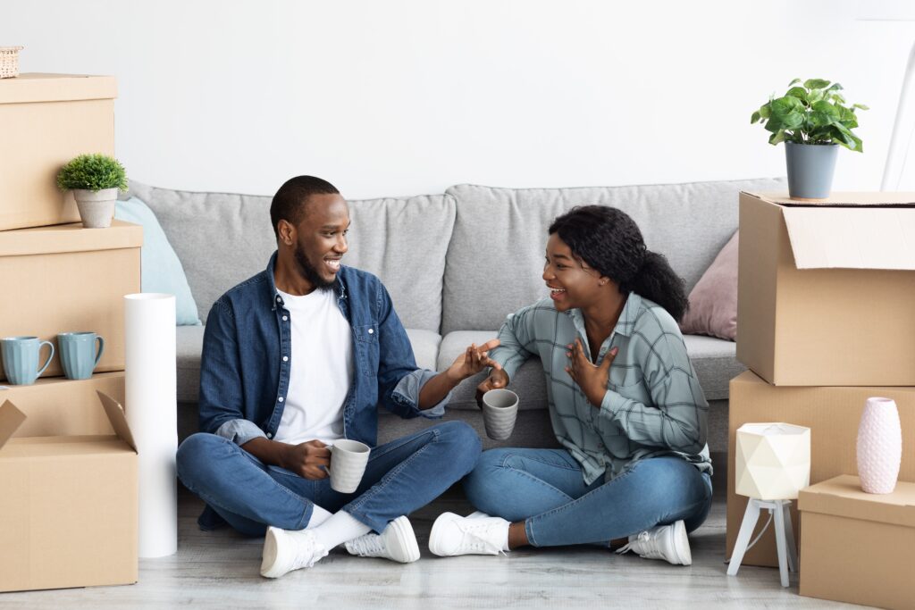 young couple sitting on floor of new house with moving boxes around them